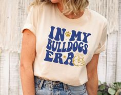 🏈 In My Bulldogs Era Shirt 🐾 | Game Day & Team Spirit Tee | Perfect Bulldogs Fan Gift 🎉 Show off your school spirit with our In My Bulldogs Era Shirt! This stylish and comfortable T-shirt is perfect for game day, cheering on your favorite team, or just representing your Bulldogs pride wherever you go. Whether you're a student, alum, or a dedicated fan, this tee is a great way to support your team and celebrate your love for the Bulldogs. Makes a fantastic gift for any Bulldogs fan! Bulldogs Team Shirt, Game Day Apparel, School Spirit Tee 👉HOW TO ORDER👈 1️⃣ Please review all the information provided before placing an order 2️⃣ Select the shirt type and size using the drop down menu. 3️⃣ Select the color of the shirt using the following drop down menu. 4️⃣ Need more Items? Add the curre Bulldogs Shirt, Bulldog Tshirt, School Shirt Designs, Mascot Shirt, Team Mascots, Team Shirt, Game Day Shirts, Team Shirts, School Shirts