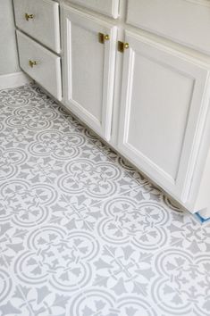 a kitchen floor with white cabinets and gray tile on the bottom, in front of an oven