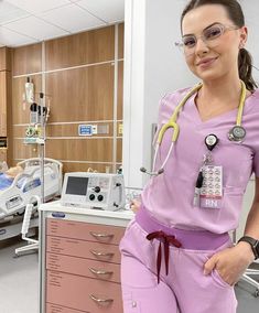 a woman in scrubs and glasses standing next to a hospital bed with medical equipment