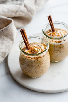 two small jars filled with pudding on top of a white plate and topped with cinnamon sticks