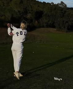 a woman is swinging her golf club at the ball on the grass in front of some trees