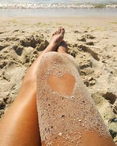 a person laying down on the beach with their feet in the sand and heart drawn in the sand