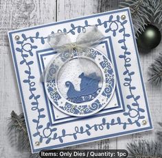 a blue and white christmas ornament hanging from a wooden table with pine branches