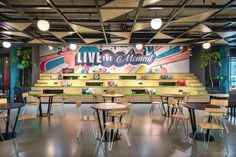 an empty cafeteria with tables and chairs in front of a live the moment sign on the wall