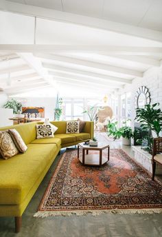 a living room with yellow couches and rugs on the floor in front of windows