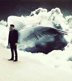 a man is standing in the snow with his wings spread out and clouds behind him