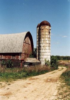 an old barn and silo on a dirt road