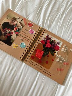 an open notebook with pictures and flowers on the cover, sitting on a bed sheet