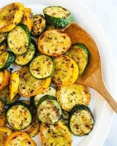 grilled zucchini and squash on a white platter with a wooden spoon