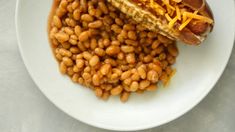 a hot dog and beans on a white plate