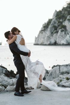 a bride and groom kissing on the beach in front of an ocean with cliffs behind them