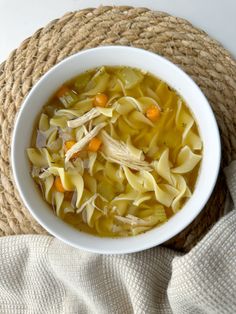 a white bowl filled with chicken noodle soup on top of a burlock