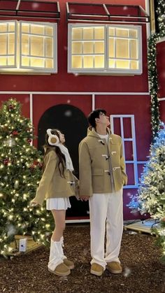 a man and woman standing in front of a red building with christmas decorations on it