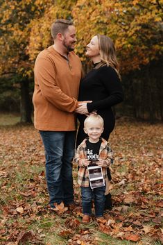 a man and woman standing next to a little boy in the middle of autumn leaves