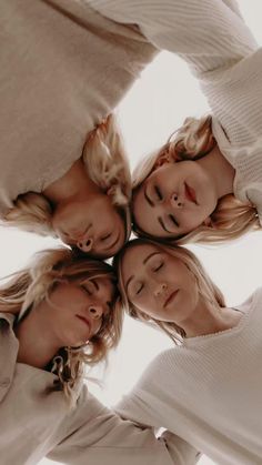 four women standing in a circle looking up at the camera with their eyes closed and hands together