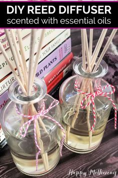 two clear glass bottles with reeds in them on top of a table next to books