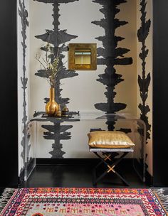 a black and white wall with a gold mirror on it's side table next to a rug