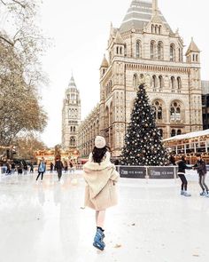 a woman is skating on an ice rink in front of a large building with a christmas tree