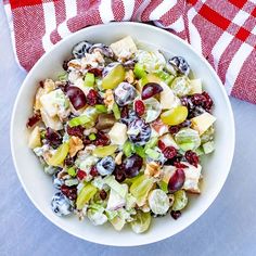 a white bowl filled with fruit salad next to a red and white checkered napkin