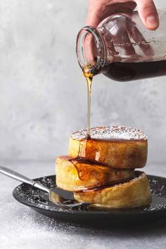 a person pouring syrup on top of some french toasts with powdered sugar and cinnamon