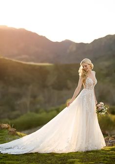 a woman in a wedding dress standing on top of a lush green field with mountains behind her