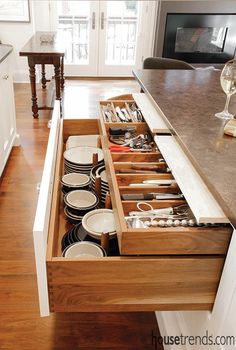 an open drawer in the middle of a kitchen with dishes and utensils inside