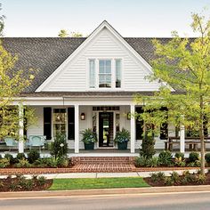 a white house with lots of windows and plants on the front porch, along with landscaping