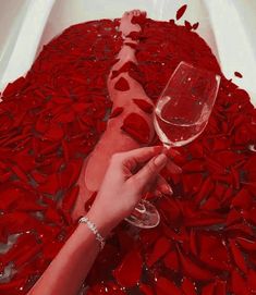 a person holding a glass of wine in front of red petals on the bathtub