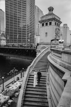 a man and woman are walking up some stairs near the water in front of tall buildings