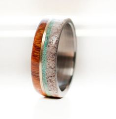 a wooden ring with green and brown inlays sits on a white surface next to a window