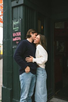 a man and woman standing next to each other in front of a green storefront