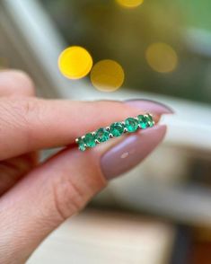 a woman's hand holding a ring with emeralds on it and gold dots in the background