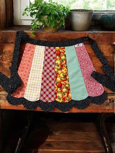 a wooden bench topped with lots of different colored pieces of cloth next to a potted plant