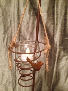 a candle is in a glass bowl on a metal stand with rope hanging from it