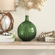 a green vase sitting on top of a wooden shelf next to a lamp and books