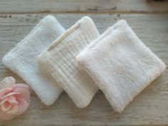 three white towels and a pink flower on a wooden surface