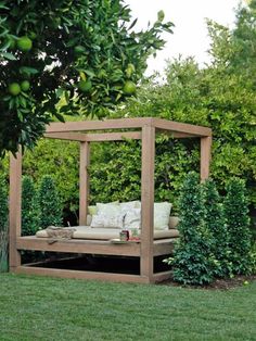 a wooden bed sitting in the middle of a lush green field next to a tree