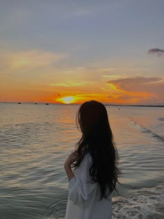 a woman standing on top of a beach next to the ocean at sunset or dawn