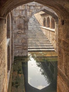 an arched doorway leading to a building with stairs and water in the pool below it