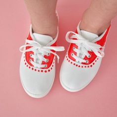 a child's feet wearing white and red shoes with laces on them, against a pink background