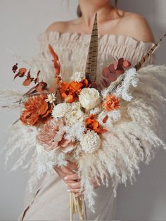 a woman wearing an off the shoulder dress holding a bouquet with feathers and flowers on it