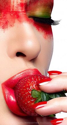 a woman with red makeup and green leaves on her lips is biting into a strawberry