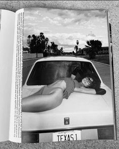 a black and white photo of a woman laying on the hood of a car