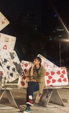 a man sitting on top of a bench next to a pile of playing cards at night