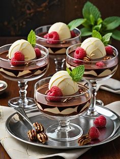 four desserts with raspberries and whipped cream in small glasses on a silver platter