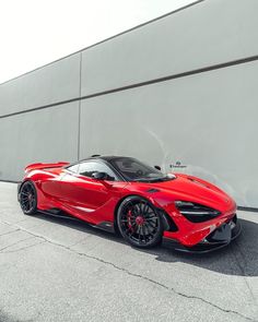 a red sports car is parked in front of a gray building with black rims