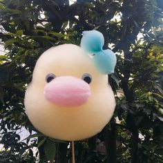 a balloon shaped like a duck with a blue bow on it's head is hanging from a tree