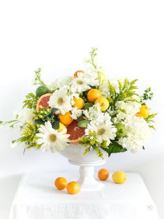 a vase filled with white flowers and oranges