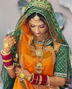 a woman dressed in an orange and green bridal outfit with jewelry on her hands