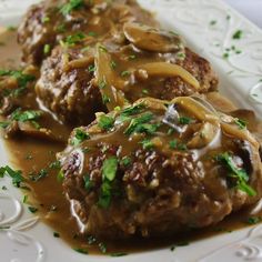 two meatballs covered in gravy on a white plate with green garnish